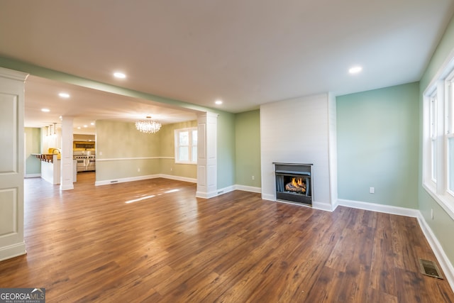 unfurnished living room with decorative columns, a large fireplace, a chandelier, and dark hardwood / wood-style flooring