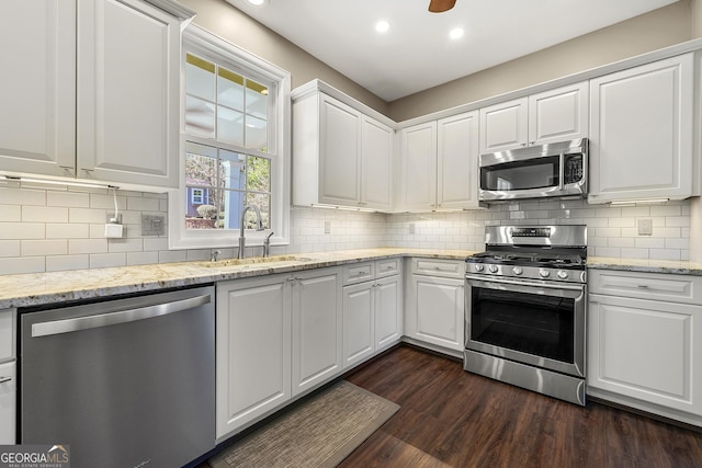 kitchen with dark wood-type flooring, a sink, white cabinetry, appliances with stainless steel finishes, and decorative backsplash