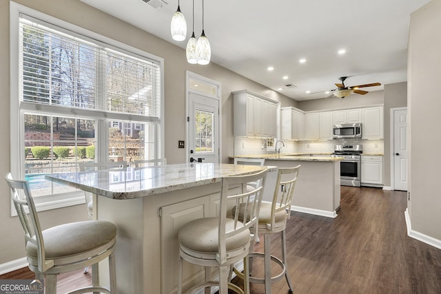 kitchen with light stone countertops, white cabinetry, appliances with stainless steel finishes, a center island, and pendant lighting