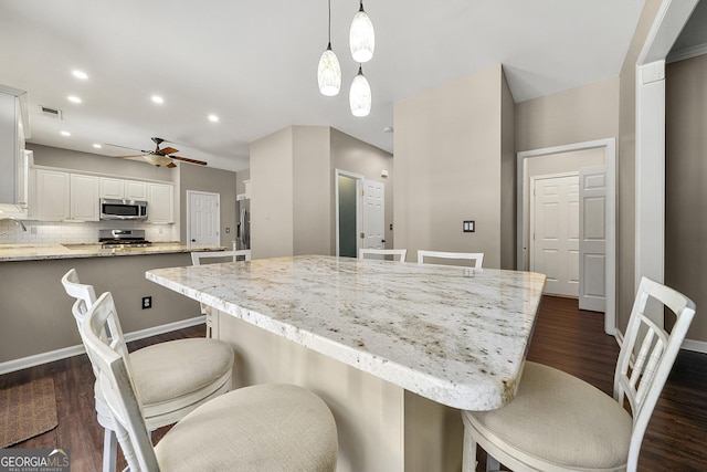 kitchen featuring light stone counters, stainless steel appliances, dark wood-style flooring, white cabinetry, and decorative light fixtures