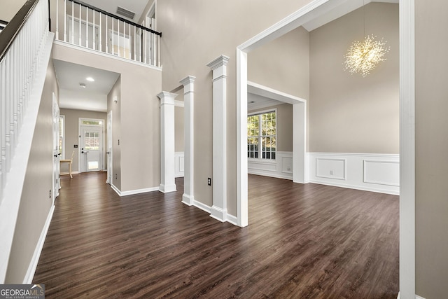 foyer entrance featuring dark wood-style flooring, visible vents, a decorative wall, a chandelier, and ornate columns