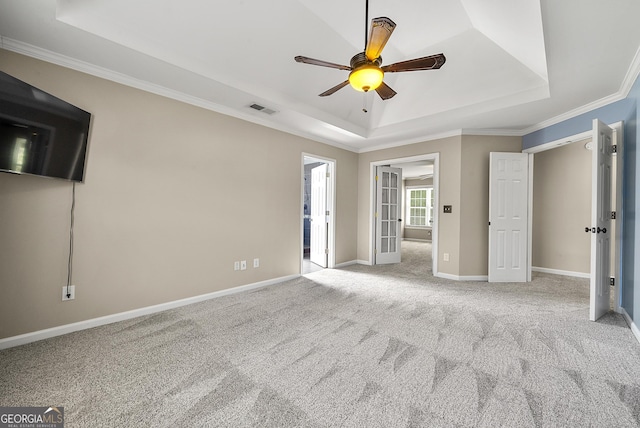 unfurnished bedroom featuring a tray ceiling, visible vents, ornamental molding, light carpet, and baseboards