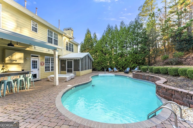 view of swimming pool featuring a sunroom, a patio area, and exterior bar