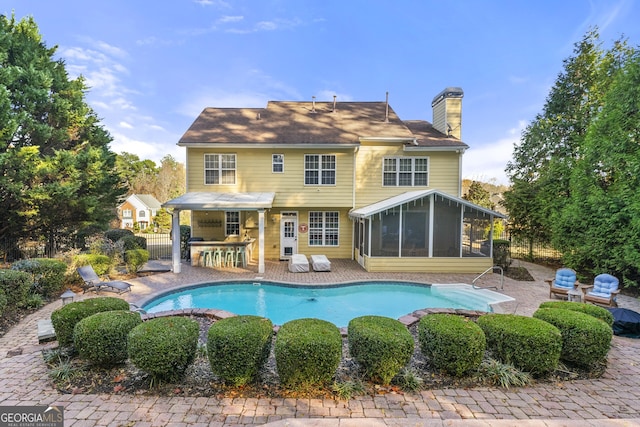 back of property with a sunroom, a chimney, outdoor dry bar, fence, and a patio area