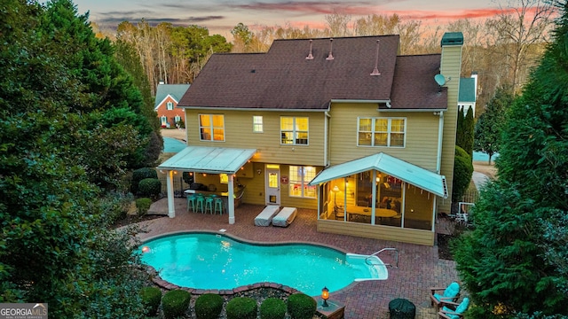 back of property featuring a patio, outdoor dry bar, roof with shingles, an outdoor pool, and a chimney