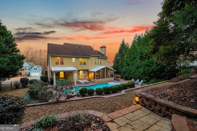 back of house at dusk with a fenced in pool, a patio, a sunroom, a chimney, and fence