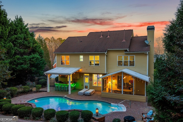 back of property with outdoor dry bar, a patio, a chimney, and an outdoor pool