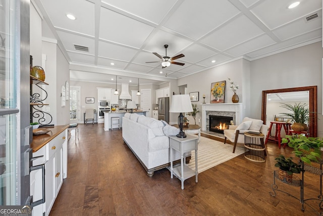 living room featuring a stone fireplace, dark wood-type flooring, visible vents, and coffered ceiling