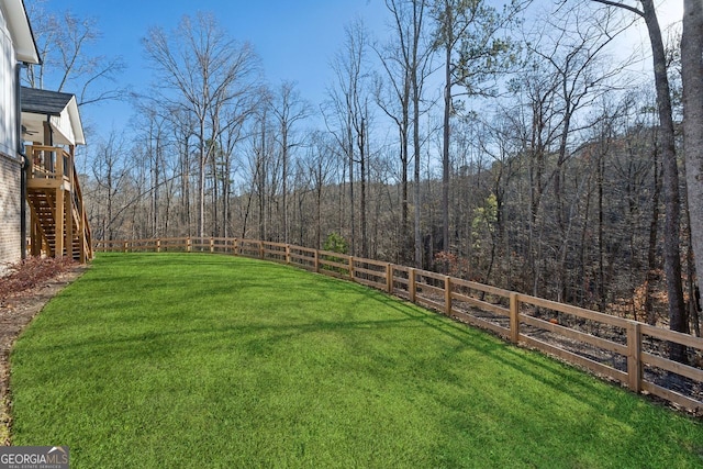 view of yard featuring a forest view, a fenced backyard, and stairway