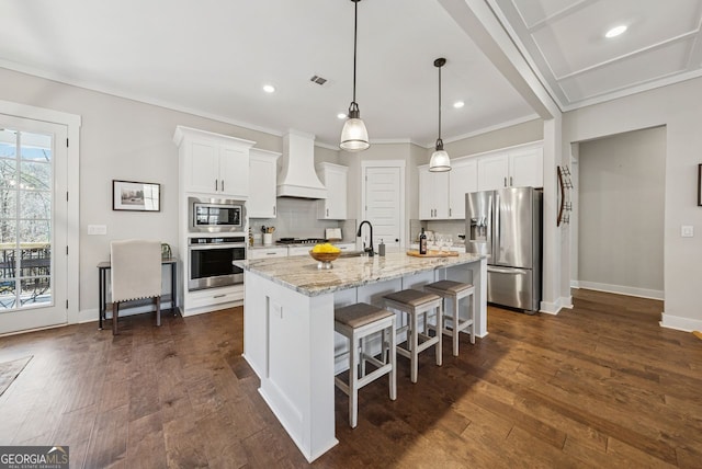 kitchen with visible vents, backsplash, custom range hood, appliances with stainless steel finishes, and a kitchen breakfast bar