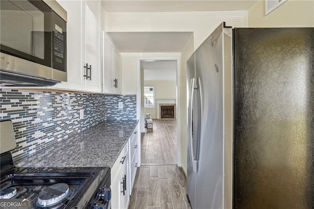 kitchen featuring white cabinets, decorative backsplash, appliances with stainless steel finishes, and dark stone counters