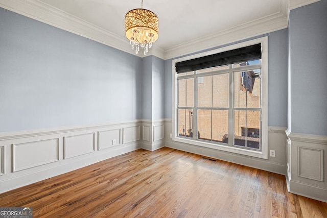 empty room with ornamental molding, light wood-type flooring, and a notable chandelier