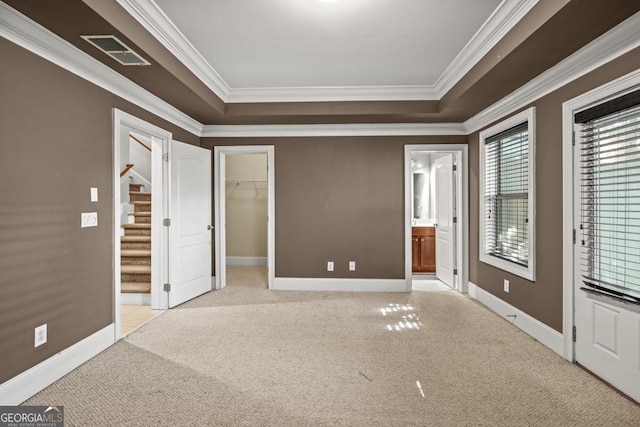 unfurnished bedroom with ensuite bathroom, a walk in closet, ornamental molding, and light carpet