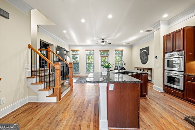 kitchen featuring a kitchen island with sink, crown molding, sink, light hardwood / wood-style floors, and stainless steel double oven