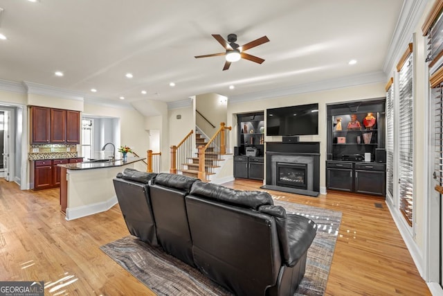 living room featuring ceiling fan, sink, ornamental molding, and light wood-type flooring