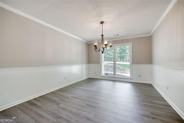 spare room featuring a textured ceiling, dark hardwood / wood-style flooring, crown molding, and a chandelier