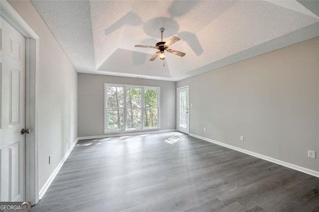 spare room with ceiling fan, dark hardwood / wood-style flooring, a textured ceiling, and a tray ceiling