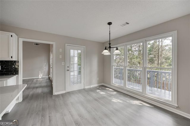 unfurnished dining area with a chandelier, a textured ceiling, and hardwood / wood-style flooring