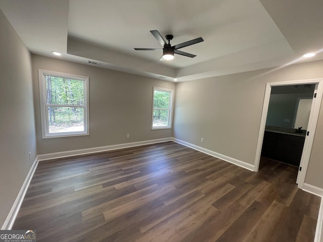 spare room with baseboards, a ceiling fan, a tray ceiling, recessed lighting, and dark wood-type flooring