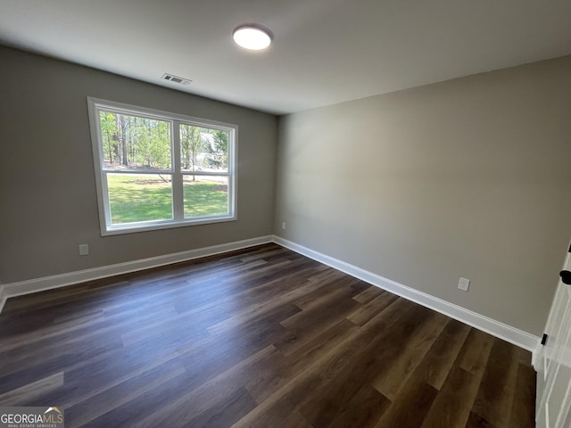 unfurnished room featuring dark wood-type flooring, visible vents, and baseboards