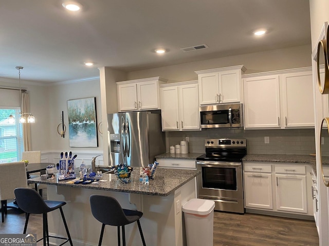 kitchen with stainless steel appliances, dark wood-type flooring, a center island with sink, dark stone countertops, and white cabinetry