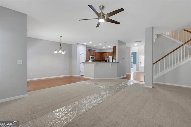 unfurnished living room featuring ceiling fan with notable chandelier and light wood-type flooring