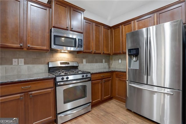 kitchen featuring dark stone counters, backsplash, stainless steel appliances, and light wood-type flooring