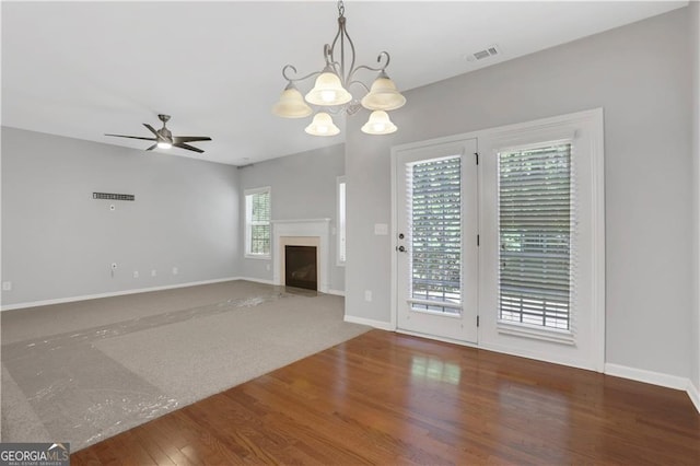 unfurnished living room featuring hardwood / wood-style floors, ceiling fan with notable chandelier, and a healthy amount of sunlight