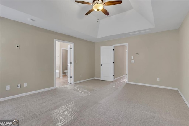 interior space with a raised ceiling, ceiling fan, and light colored carpet