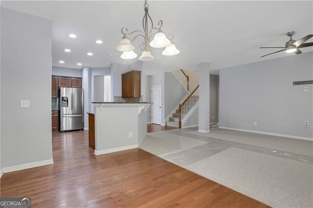 kitchen featuring kitchen peninsula, ceiling fan with notable chandelier, decorative light fixtures, hardwood / wood-style flooring, and stainless steel fridge with ice dispenser