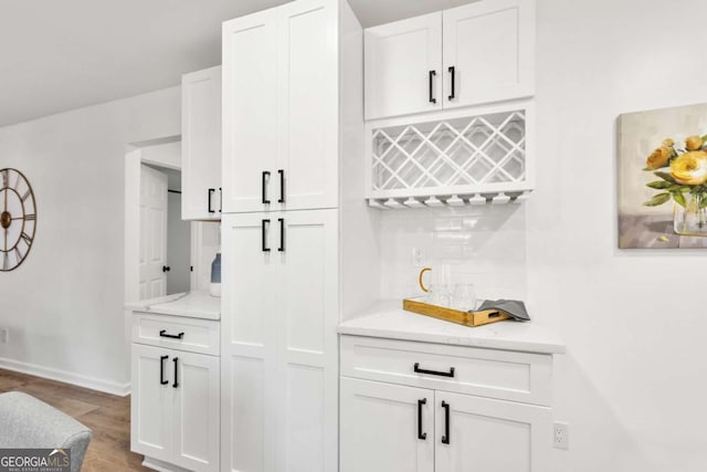 bar with decorative backsplash, light stone counters, hardwood / wood-style floors, and white cabinets