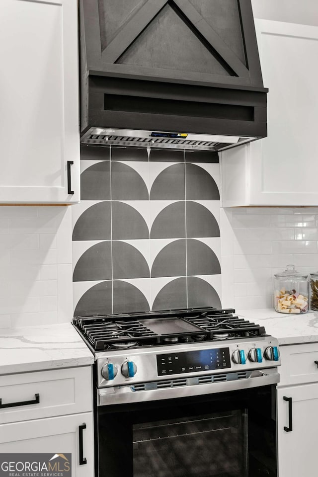 interior details with backsplash, stainless steel gas stove, range hood, light stone counters, and white cabinetry