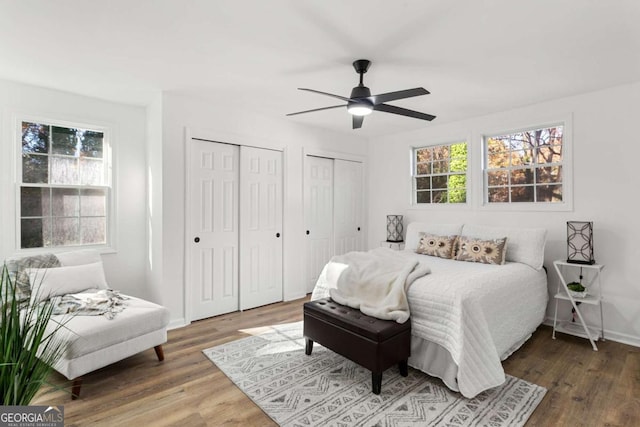 bedroom with hardwood / wood-style floors, two closets, and ceiling fan