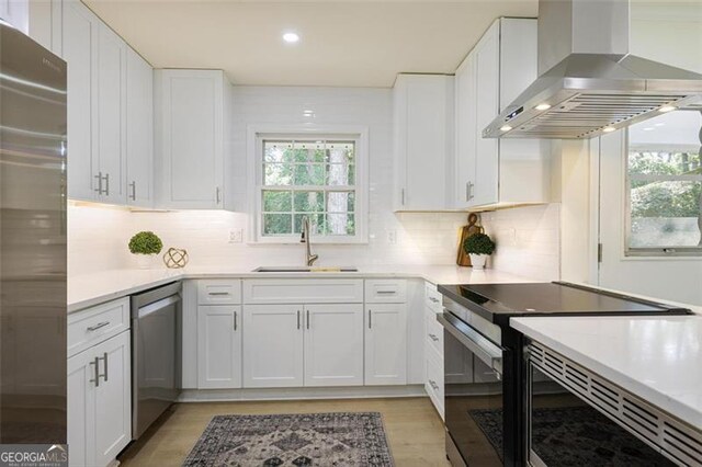 kitchen with appliances with stainless steel finishes, tasteful backsplash, white cabinetry, and wall chimney exhaust hood