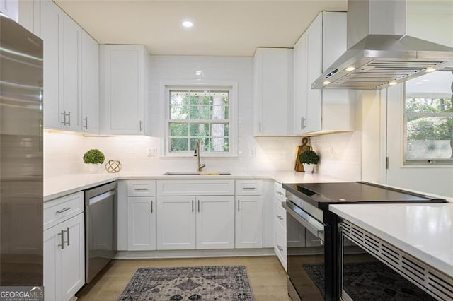 kitchen with light countertops, appliances with stainless steel finishes, white cabinets, a sink, and island range hood