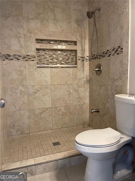 bathroom featuring a tile shower, toilet, and tile patterned floors