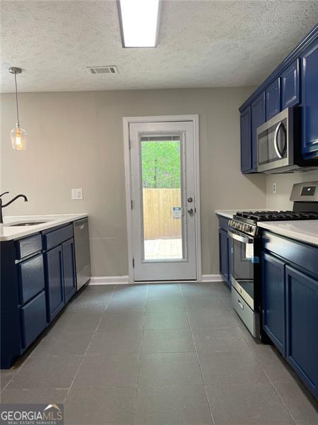 kitchen featuring blue cabinetry, sink, stainless steel appliances, pendant lighting, and a textured ceiling