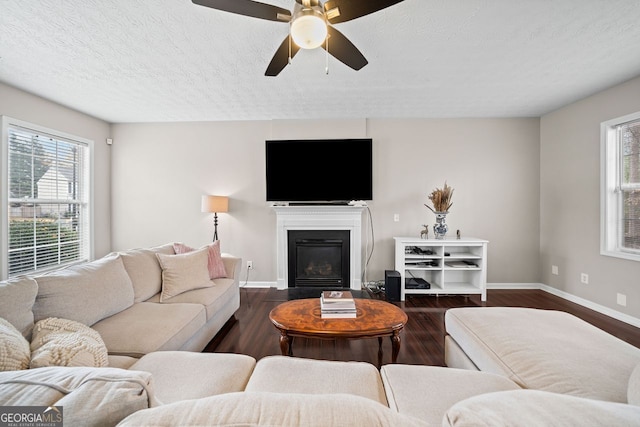 living room with a textured ceiling, ceiling fan, and dark wood-type flooring