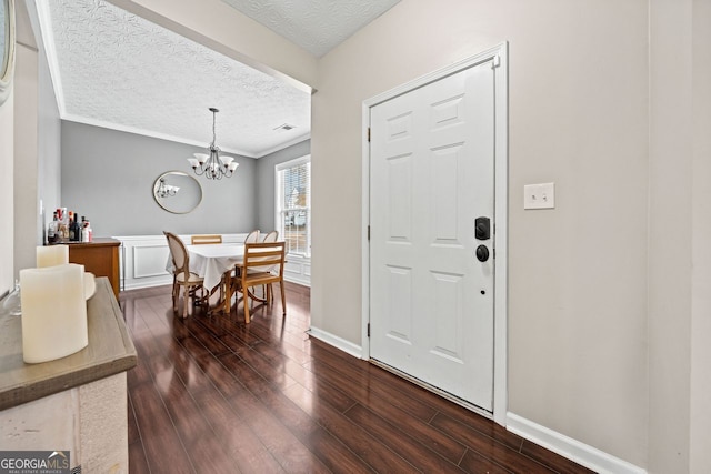 entrance foyer featuring dark hardwood / wood-style floors, ornamental molding, a textured ceiling, and an inviting chandelier