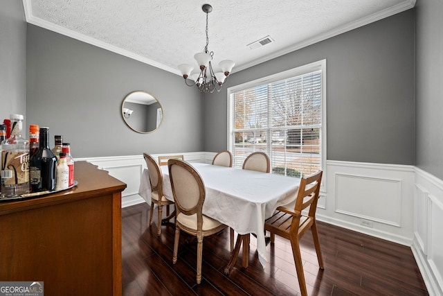 dining area featuring dark hardwood / wood-style flooring, an inviting chandelier, a textured ceiling, and ornamental molding