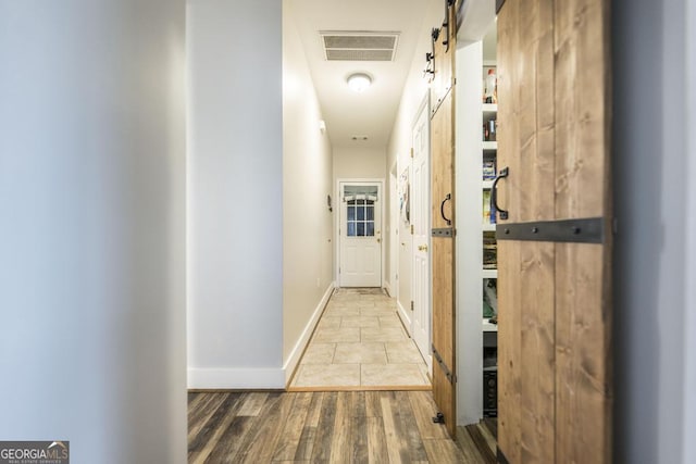 corridor featuring a barn door, wood finished floors, and baseboards