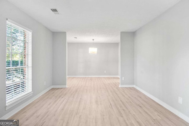 spare room featuring a notable chandelier and light hardwood / wood-style flooring