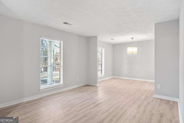 unfurnished room featuring a textured ceiling, light wood-type flooring, an inviting chandelier, and plenty of natural light