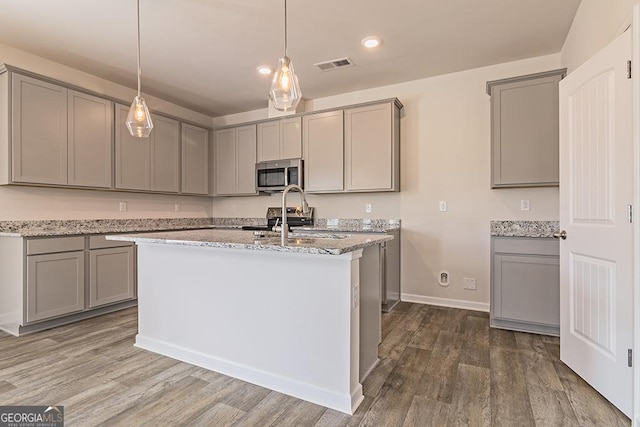 kitchen with appliances with stainless steel finishes, light stone counters, gray cabinetry, sink, and hardwood / wood-style floors