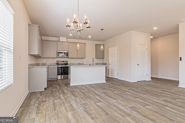 kitchen with gray cabinetry, pendant lighting, light wood-type flooring, an island with sink, and stainless steel appliances