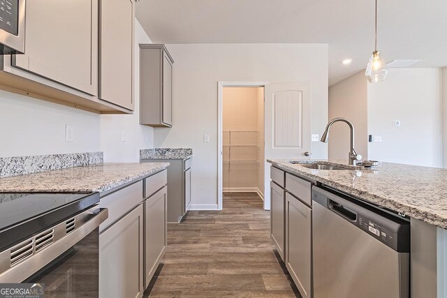 kitchen with light stone countertops, stainless steel appliances, sink, gray cabinets, and dark hardwood / wood-style floors