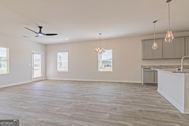 kitchen featuring gray cabinets, light stone counters, pendant lighting, and ceiling fan with notable chandelier