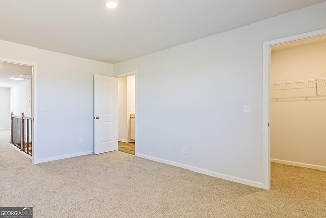 unfurnished bedroom with light colored carpet, a walk in closet, and a closet