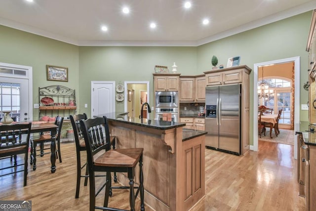 kitchen featuring a breakfast bar, ornamental molding, stainless steel appliances, and an island with sink