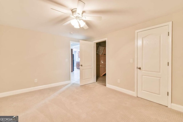 unfurnished bedroom featuring a closet, a walk in closet, light colored carpet, and ceiling fan